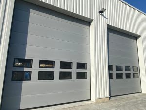 Porte de garage sectionnelle industrielle avec hublots transparents, installation dans un entrepôt moderne